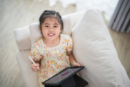 Asian child girl using pen and touch drawing on tablet display screen. Baby smiling funny time to use tablet. Too much screen time. Cute girl watching videos while tv, Internet addiction concept.の写真素材
