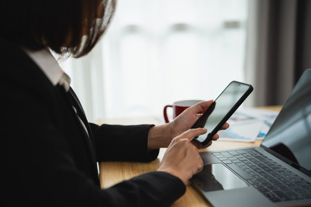 Businesswoman using smartphone after working with laptop on table, woman using mobile phone search or social media or shopping online or stock or crypto currency. Smart phone conversation conferrence.の写真素材