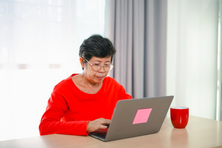 Senior old asian woman working after retirement using laptop at home. Old freelancer working or learning new technology on laptop in living room. Retirement activity concept.の写真素材