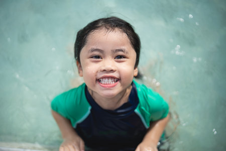 Asian child kid girl smiling funny wearing swimming suit to swimming or leaning training on swimming pool in water park. Water activity for children on summer holiday.の写真素材