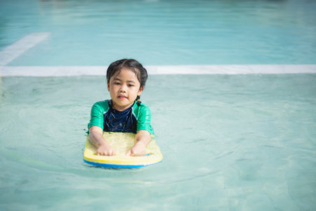 Asian child kid girl smiling funny wearing swimming suit using kick board to swimming or leaning...