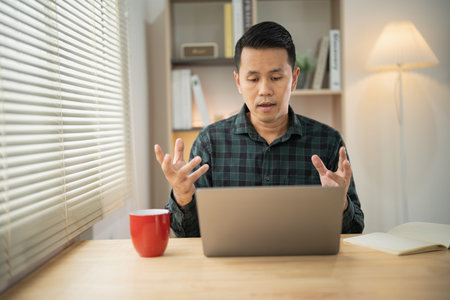 Asian freelance business man working talking making video call in home office, using laptop,...