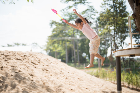 Asian girl children jumping and playing sand on the playground in the cafe for kids. Little girl playing in the sand on the playground. Healthy active baby outdoors plays games concept.の写真素材