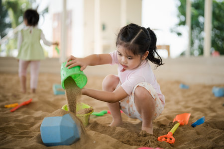 Asian girl children playing sand on the playground in the cafe for kids. Little girl playing in the sand on the playground. Healthy active baby outdoors plays games concept.の写真素材