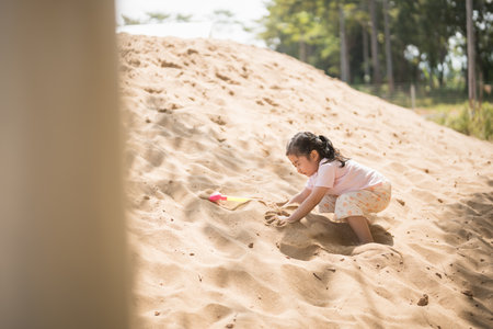 Asian girl children playing sand on the playground in the cafe for kids. Little girl playing in the sand on the playground. Healthy active baby outdoors plays games concept.の写真素材