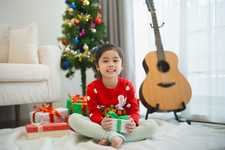 Christmas, x-mas, winter concept. Asian baby child girl holding gift boxes smiling happy cheerful. Celebrates the Happy New Year near the Christmas tree in a living room at home.の写真素材