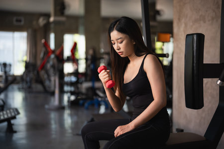 Asian fit sportswoman smiling and working out excercise weights with dumbbells at the fitness gym. asian woman wearing sportwear doing exercise to burn fat at gym. Sport woman fitness concept.の写真素材