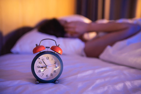 Close up of alarm clock. depressed woman sadly laying on the bed in the bedroom. Sad asian women suffering depression insomnia awake and sit alone on the bed in bedroom. Wake up late.の写真素材