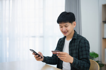 Man holding credit card and using mobile to shopping online. asian man working at home. Online shopping, e-commerce, internet banking, spending money, working from home concept.の写真素材