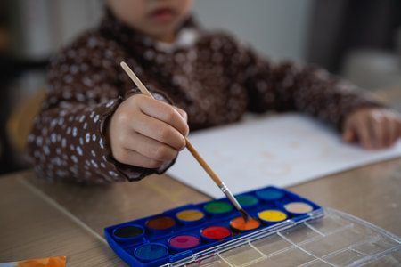 Close up hand of cute little asian baby smiling painting with colorful paints using watercolor. Asian girl using paintbrush drawing color. Baby activity lifestyle concept.の写真素材