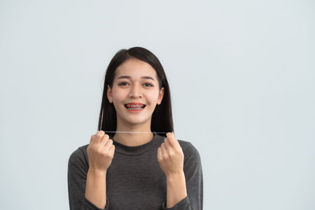Asian woman braces using dental floss. Teeth braces on the white teeth of women to equalize the...