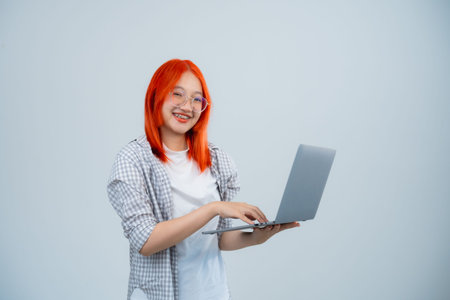 Teen woman wearing glasses holding and typing laptop isolated on white or grey background, women...