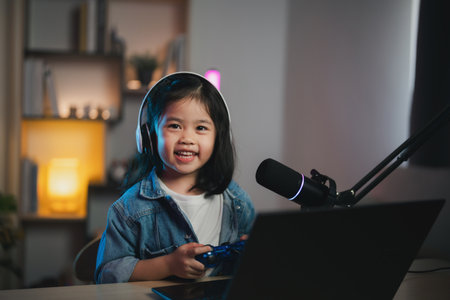 Asian influencer young girl smile cheerful using joystick playing game live streaming greeting video conference with laptop and wearing headphone. Children streaming cast game online concept.の写真素材