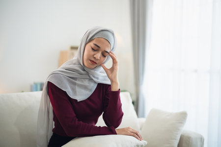 Muslim islam Asian woman wearing hijab depressed sadly serious  having stressful depression sad time sitting on sofa in the living room at home. Depression woman sad serios health mental concept.の写真素材