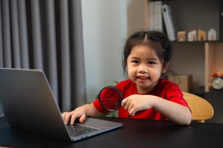 Asian baby kid girl holding magnifying glass and using laptop education to get good ideas, children and school concept - happy smiling student girl learning studying. Education development concept.の写真素材