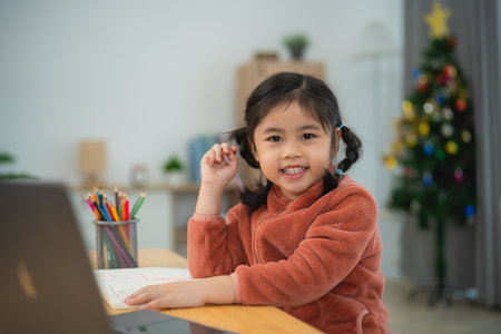 Happy Child Drawing with Color Pencils at Home. A cheerful young girl with pigtails draws contentedly with color pencils, seated at her home desk. Education for kids concept.の写真素材