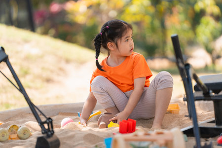 Asian girl children playing sand on the playground in the cafe for kids. Little girl playing in the sand on the playground. Healthy active baby outdoors plays games concept.の写真素材