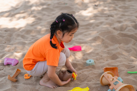 Asian girl children playing sand on the playground in the cafe for kids. Little girl playing in the sand on the playground. Healthy active baby outdoors plays games concept.の写真素材