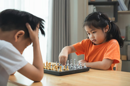 Two children playing a game of chess. One is wearing a white shirt and the other is wearing an orange shirtの写真素材