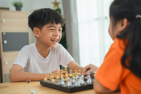 Two children playing a game of chess. One is smiling and the other is frowning. The boy in the white shirt is smiling and the girl in the orange shirt is frowningの写真素材