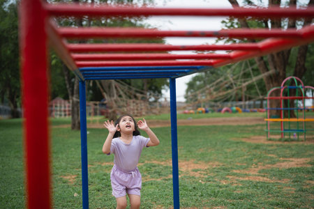 Asian little girl is looking up at a red and blue structure in a park. She is wearing a purple shirt...