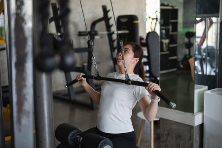 A woman is working out on a weight machine. She is lifting a bar with a black handle
