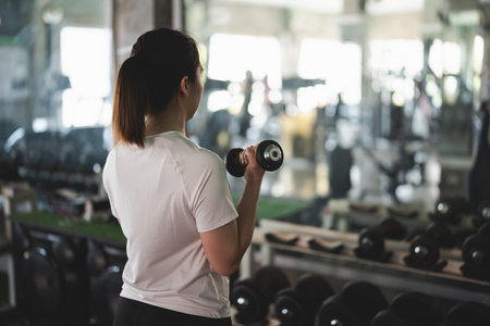 A woman is lifting weights in a gym. She is wearing a white shirt and has a ponytailの写真素材