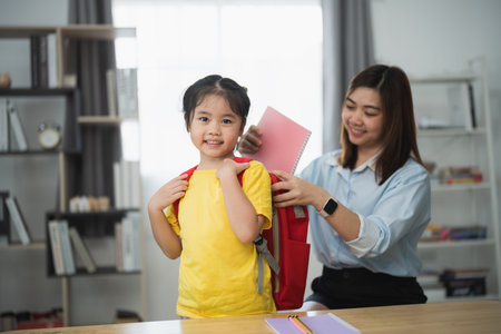 Asian young girl in a yellow shirt is getting her backpack ready to go to school