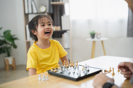 Asian young girl is playing a game of chess with an adult. She is smiling and laughing as she playsの写真素材