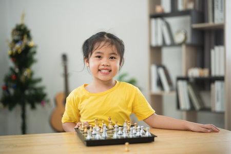 Asian young girl is sitting at a table with a chess board in front of her. She is smiling and she is enjoying herselfの写真素材