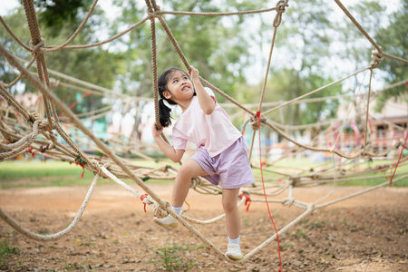 Asian young girl is playing on a rope course, climbing up and down the ropes. The scene is lively and playful, with the girl enjoying herself as she navigates the courseの写真素材