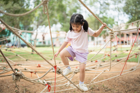 Asian young girl is playing on a rope course, climbing up and down the ropes. The scene is lively and playful, with the girl enjoying herself as she navigates the courseの写真素材