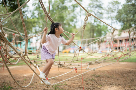 Asian young girl is playing on a rope course, climbing up and down the ropes. The scene is lively and playful, with the girl enjoying herself as she navigates the courseの写真素材