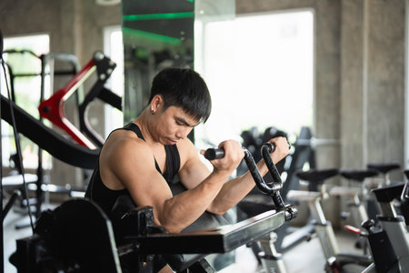Asian man is working out in a gym, lifting weights and doing pushups. The gym is filled with various exercise equipment, including a bench and a machine. The atmosphere is energetic and focusedの写真素材