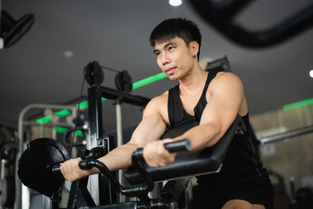 Asian man is working out in a gym, lifting weights and doing pushups. The gym is filled with various exercise equipment, including a bench and a machine. The atmosphere is energetic and focusedの写真素材