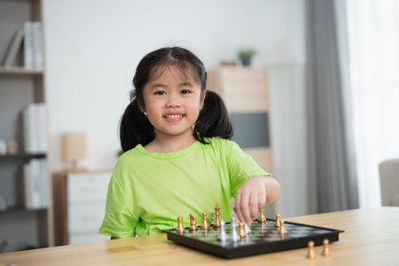 A young girl is playing a game of chess with a smile on her face. She is wearing a green shirt and is sitting at a table with a chess board in front of herの写真素材