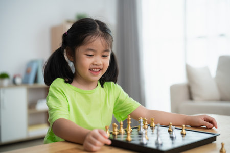 A young girl is playing a game of chess with a board and pieces. She is smiling and she is enjoying herselfの写真素材