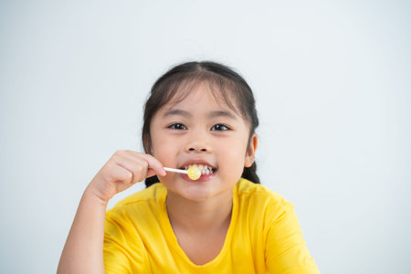 Asian young girl is smiling while holding a toothbrush. She is wearing a yellow shirt. Concept of...