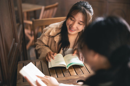 Two women sitting at a table, one reading a book. Scene is friendly and relaxedの写真素材