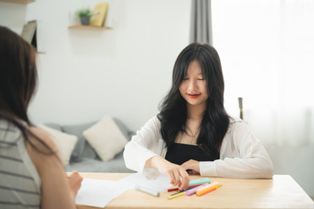 A woman is sitting at a table with a piece of paper and a box of markers. She is looking at the paper and seems to be in a focused or serious moodの写真素材