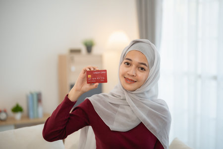 Muslim islam woman with hijab wearing a grey scarf is holding a red card. She is smiling and she is happyの写真素材