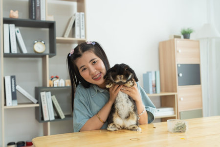 Asian girl is holding a rabbit on a table. The rabbit is black and white. The girl is smiling