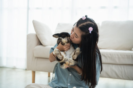 Asian girl is holding a rabbit in her arms. The rabbit is white and black. The girl is wearing a blue shirtの写真素材