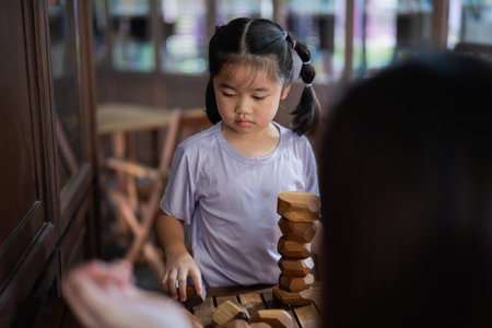 Asian young girl is playing with wooden blocks. She is wearing a purple shirt and has her hair in...