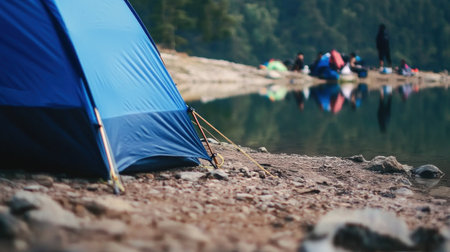 A peaceful campsite by a serene lake, featuring a blue tent, nature's beauty, and reflections, perfect for outdoor enthusiasts seeking relaxation.の素材