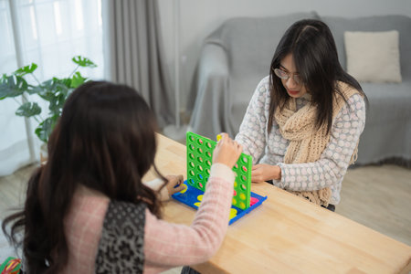 Two women engage in a friendly game of Connect Four at a cozy table in a modern home interior, showcasing fun, strategy, and friendship in indoor leisure.の写真素材