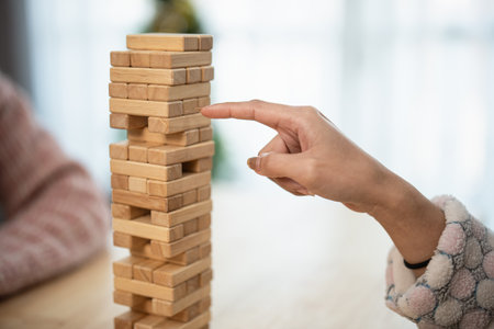 Hand Reaching for a Block in a Tower of Wooden Game Pieces, Capturing the Tension of a Competitive Family Game Night Experienceの写真素材