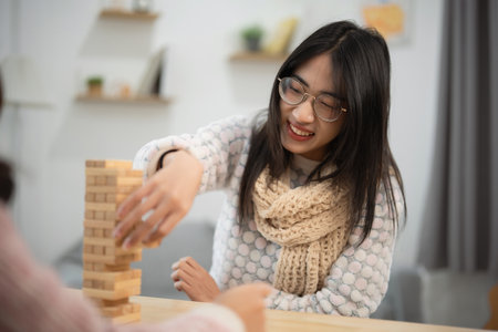 Woman in Cozy Sweater Playing wood block Game with Friends in Bright, Modern Living Room, Enjoying Fun and Laughter During Leisure Time Togetherの写真素材