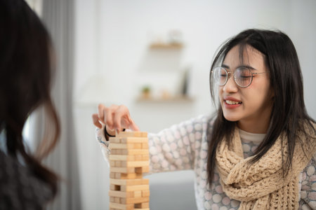 Young woman with glasses playing wood block game, enjoying time with friends in cozy indoor setting, smiling and focused on winning while stacking wooden blocksの写真素材