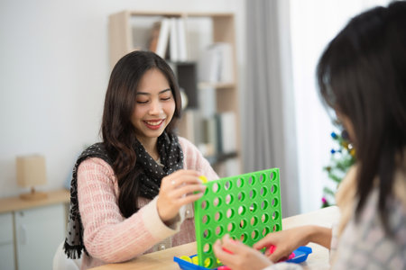 Joyful friends playing a connection game indoors in a cozy living room, smiling and enjoying quality time, surrounded by holiday decorations and natural lightの写真素材